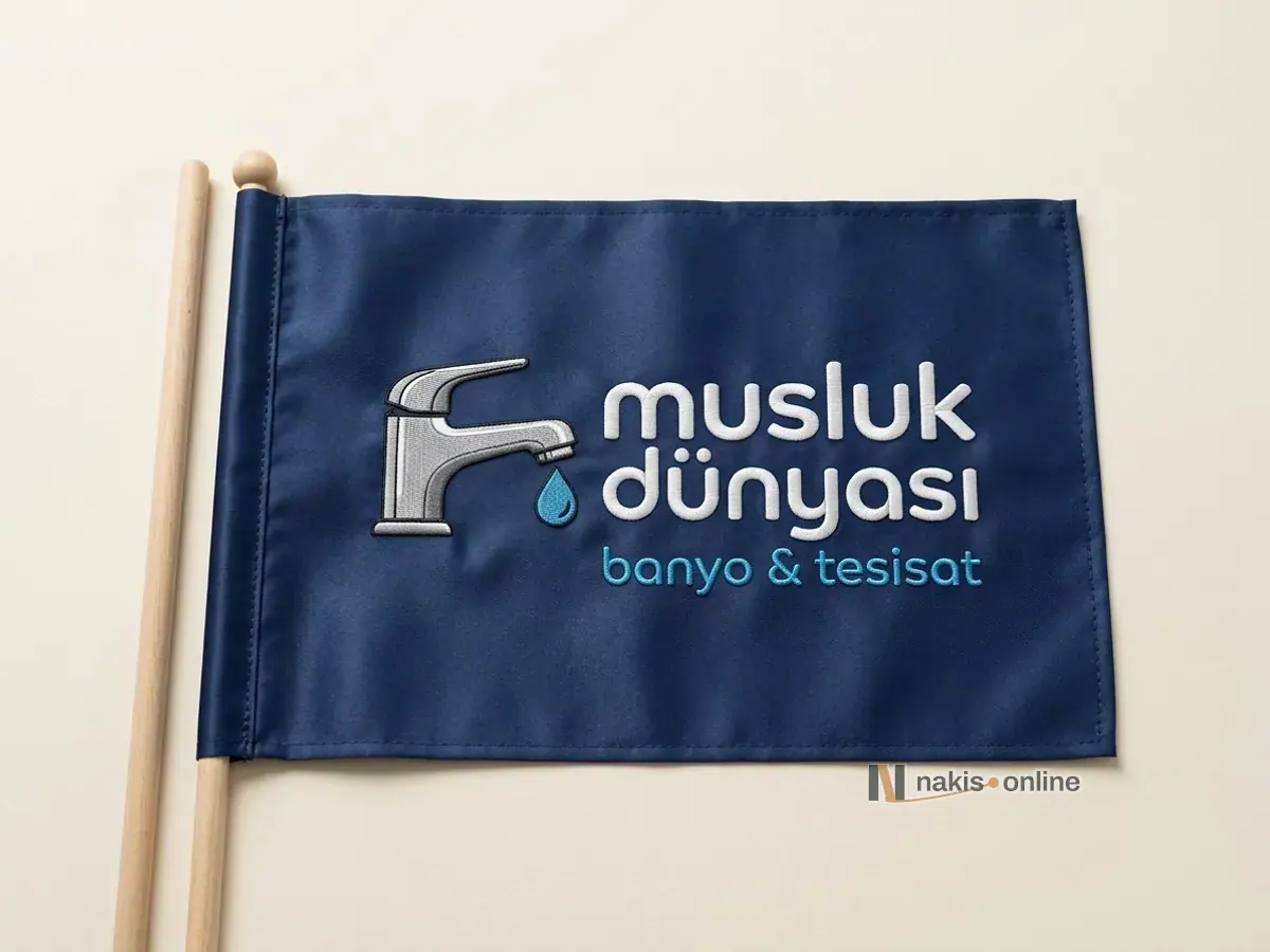 Stüdyo zemininde düz serilmiş lacivert saten masa bayrağı ve ince ahşap direk; ortasında gri musluk ve mavi su damlası simgesiyle bir banyo ve tesisat mağazasının beyaz harfli logosu