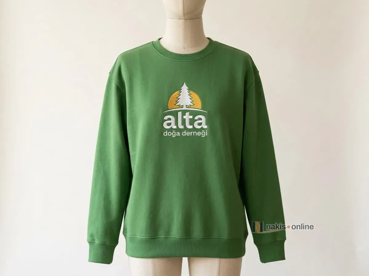 Yeşil bisiklet yaka sweatshirt: göğüs ortasında beyaz çam ağacı, arkasında sarı yarım güneş ve beyaz harflerle bir doğa derneğinin arması